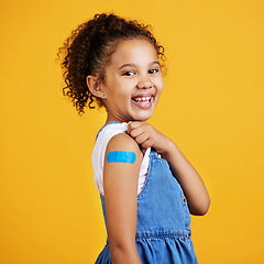 Image showing Happy, portrait and child with a plaster in a studio for a wound, sore or injury on her arm. Happiness, smile and healthy girl kid model posing with a bandage after a vaccination by yellow background