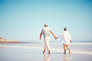 Image showing Holding hands, beach and an old couple walking outdoor in summer with blue sky mockup from behind. Love, romance or mock up with a senior man and woman taking a walk on the sand by the ocean or sea