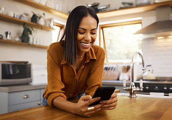 Image showing Happy woman, phone text and kitchen in a home reading a web app. House, female and smile of a young person with joy resting on a counter top table feeling relax typing with mobile networking