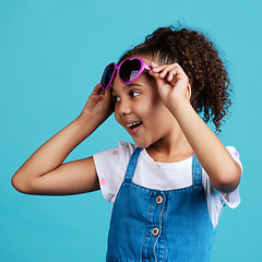 Image showing Happy, smile and of a child with sunglasses in studio with positive, energy and excited face expression. Happiness, childhood and girl kid model with funky, trendy and cool glasses by blue background