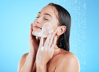 Image showing Shower, facial and woman washing face with soap on blue background for grooming, cleaning and wellness. Skincare, bathroom and happy girl with foam product for hygiene, hydration and beauty in studio