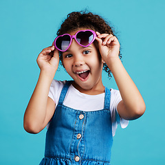 Image showing Happy, sunglasses and portrait of a child in studio with a positive, shocked and excited face expression. Happiness, surprise and girl kid model with funky, trendy and cool glasses by blue background