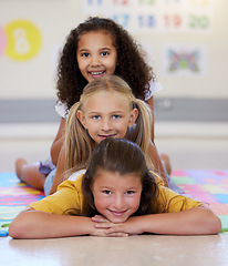 Image showing School kids, lying together and pile on floor, portrait and classroom for smile, solidarity or diversity. Girl, children and class at academy, happy or multicultural friends with support for learning