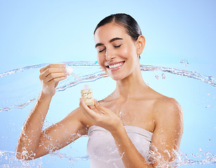 Image showing Happy woman, dropper and water splash for skincare serum, product or cream against a blue studio background. Calm female smile holding pipette for beauty cosmetics, essential oil or facial treatment