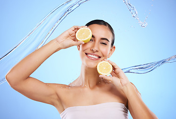 Image showing Vitamin c, lemon and water splash with portrait of woman in studio for natural cosmetics, nutrition and detox. Glow, fruits and hydration with female on blue background for diet, face and skincare