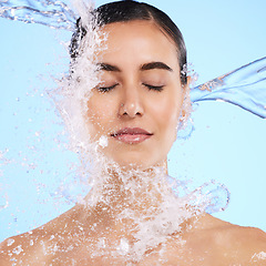 Image showing Water splash, face and skincare with a woman in studio on a blue background for hygiene or hydration. Relax, beauty and cleaning with an attractive young female in the shower for self care