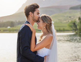 Image showing Love, wedding with a bride and groom kissing by a lake outdoor in celebration of their marriage for romance. Water, summer and kiss with a newlywed couple bonding together in tradition after ceremony