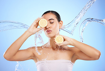 Image showing Beauty, skincare and water splash with woman and lemon in studio for natural cosmetics, nutrition or mockup. Wet, fruits and hydration for female on blue background for diet, face or citrus vitamin c