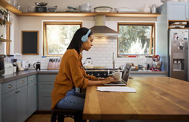 Image showing Home, remote work and business woman on laptop for research project, strategy and planning in kitchen. Freelancer, focus and girl with headphones for music with documents, computer and working online