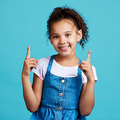 Image showing Portrait, point and mockup with a girl on a blue background in studio showing product placement space. Kids, marketing and advertising with an adorable female child pointing at branding indoor