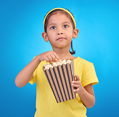 Image showing Popcorn, eating and watching movie with girl in studio for food, cinema and relax. Television, focus and film with child and snack for streaming, subscription and tv isolated on blue background