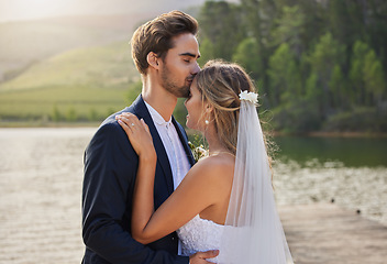 Image showing Couple, wedding and forehead kiss by lake on romantic honeymoon or getaway together in nature. Man kissing woman on head and hugging for marriage, relationship or loving embrace in the outdoors