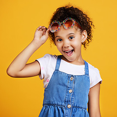 Image showing Girl child, smile and sunglasses in studio portrait for summer style or happy by yellow background. Mixed race model, female kid or fashion frame on face for surprise expression, eye care and youth