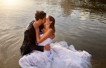 Image showing Wedding, kiss and couple in the water of a lake to celebrate their sunset marriage outdoor in nature. Happy, love and young wet man and woman being intimate for romantic playful outdoor celebration.