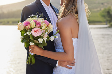 Image showing Flower bouquet, wedding and hug with couple in nature for commitment, romantic ceremony or union event. Outdoor lake, love and countryside marriage of man and woman hugging in solidarity and support