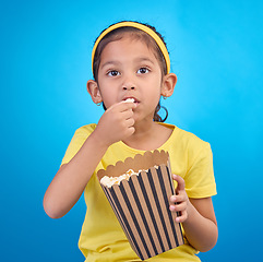 Image showing Popcorn, eating and focus with girl in studio for food, cinema and relax. Television, movie and film with child and snack for streaming service, subscription and tv isolated on blue background