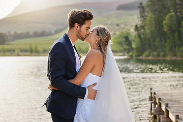 Image showing Love, wedding and a married couple kissing by a lake outdoor in celebration of their marriage for romance. Water, summer or kiss with a bride and groom bonding together in tradition after ceremony