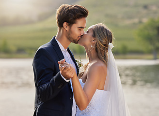 Image showing Wedding kiss, couple and lake with a bride feeling love, care and support from marriage together. Nature, happiness and holding hands of young people with romance from trust and commitment event