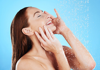 Image showing Shower, water and happy woman smile in studio, blue background and cleaning for hygiene. Young female model washing with wet drops for beauty, skincare and grooming for self care, wellness or routine