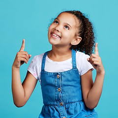 Image showing Happy, looking and a child pointing in a direction isolated on a blue background in a studio. Smile, thinking and a young girl showing up with a hand gesture, advertising and counting on a backdrop