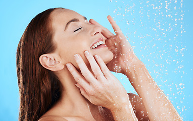 Image showing Shower, water and smile of woman in studio, blue background and cleaning for hygiene. Happy female model washing with wet drops for beauty, skincare and grooming for self care, wellness and routine