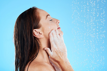 Image showing Shower, water and woman soap on face in studio, blue background and hygiene cleaning. Relax female model washing facial with wet drops, foam and beauty of skincare cosmetics, self care and backdrop