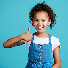 Image showing Happy, portrait and girl child with thumbs up in a studio with success, happiness and achievement. Smile, positive and face of a kid with a satisfaction or approval hand gesture by a blue background.