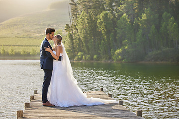 Image showing Wedding couple, kissing and hug by lake for love affection, intimate or romantic honeymoon getaway in nature. Man and woman kiss in happiness for marriage relationship or loving embrace outdoors