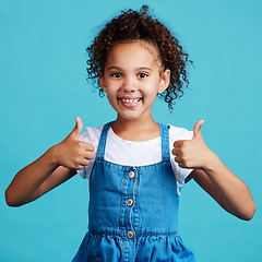 Image showing Smile thumbs up and portrait of a kid in a studio with success, happiness and achievement. Happy, positive and face of a girl child with a satisfaction or approval hand gesture by a blue background.