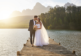 Image showing Kiss, romantic and a married couple on a pier over a lake in nature with a forest in the background after a ceremony. Wedding, love or water with a bride and groom in celebration of marriage outdoor