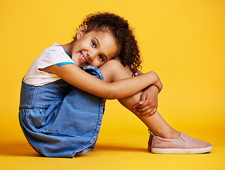 Image showing Portrait, happy and girl child on studio floor for children fashion, playful and sweet against yellow background. Face, little and smile by kid with self love, pose and relax while sitting isolated