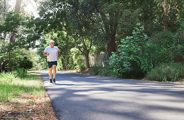 Image showing Man, exercise and outdoor in nature for run, workout and training on road with trees for fitness. Happy senior male person smile and thinking of cardio health and wellness while running in retirement