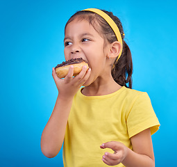 Image showing Donut, eating and sweet with girl in studio for junk food, sugar and happiness. Snack, cake and cute with face of child and dessert for candy diet and chocolate isolated on blue background