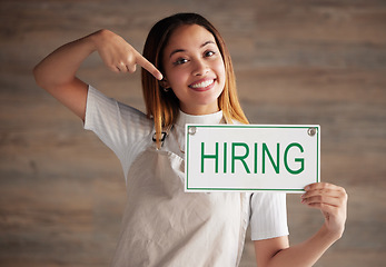 Image showing Happy woman, portrait and pointing to hiring sign for small business recruitment, career or job opportunity against studio background. Female entrepreneur with apron holding billboard poster for hire