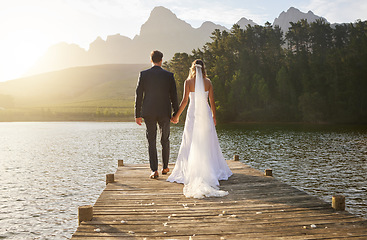 Image showing Love, wedding and back of couple by a lake standing, bonding and holding hands on the pier. Nature, romance and young bride and groom in an intimate moment together outdoor on a romantic marriage day