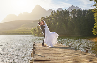 Image showing Kiss, dance and a married couple on a pier over a lake in nature with a forest in the background after a ceremony. Wedding, love or water with a bride and groom in celebration of marriage outdoor