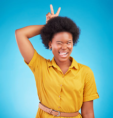 Image showing Silly, peace sign and woman in a studio feeling fun, playful and funny with a blue background. V hand gesture, bunny ears and tongue out for comedy with a young female model smile with happiness