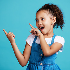 Image showing Wow, pointing and a girl on a blue background in studio for marketing with product placement space. Kids, surprise and hand gesture with an adorable little female child showing mockup for advertising