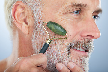 Image showing Elderly man, jade roller and face for skincare with smile, self care and wellness in studio by white background. Elderly model, facial massage and beauty with stone product, cosmetic and dermatology