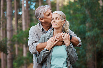 Image showing Hiking, kiss and senior couple with love in a forest, relax and hug while standing in nature park together. Caring, embrace and sweet, elderly man with woman on retirement vacation in the woods