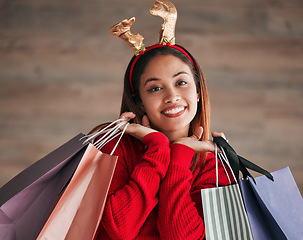 Image showing Shopping bags, portrait and woman with a christmas headband for a festive or holiday celebration. Happy, smile and face of a female model with gifts or presents with xmas reindeer ears for an event.