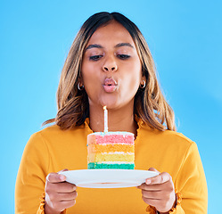 Image showing Birthday cake, candle blowing and woman in a studio with celebration and dessert. Party food, isolated and blue background of a young female with sweet and rainbow treat with surprise and plate