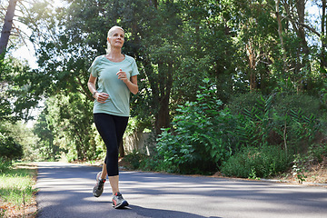 Image showing Fitness, health and a running senior woman on a road through a forest or park for cardio and endurance. Exercise, mockup and workout with a mature female runner or athlete training outdoor in nature