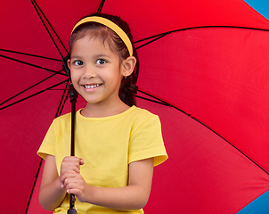 Image showing Winter, happy and portrait of a child with an umbrella, open and red while isolated in a studio. Smile, safety and a young girl protecting from the rain, bad weather and the cold for insurance