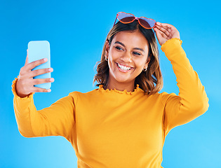 Image showing Woman, face and smile in studio for selfie, social media or vlog in happiness and style against a blue background. Happy isolated female influencer smiling for picture photo, memory or online post