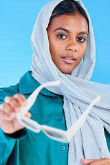 Image showing Fashion glasses, face portrait and muslim woman with hijab, trendy designer brand or casual outfit style. Gen z aesthetic, Islamic person giving sunglasses and Arab female on blue background studio