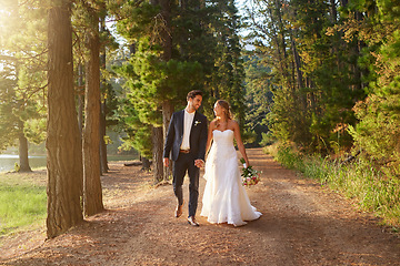 Image showing Wedding, happy and couple walking in park, nature and forest for union celebration, care and marriage. Bride, groom and walk in woods, love and commitment to support, trust and smile together outdoor