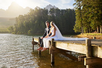 Image showing Forest, lake and a married couple on a pier in celebration together after a wedding ceremony of tradition. Marriage, love or romance with a bride and groom sitting outdoor while bonding in nature