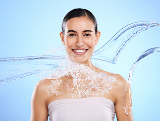 Image showing Water splash, portrait and woman shower in studio, blue background and healthy beauty of wellness skincare. Happy female model, wet and cleaning for hygiene, hydration and smile on color backdrop