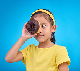 Image showing Donut, eye and cover of girl in studio for junk food, sugar and happiness. Snack, cake and cute with face of young child and dessert for eating, sweet and chocolate isolated on blue background